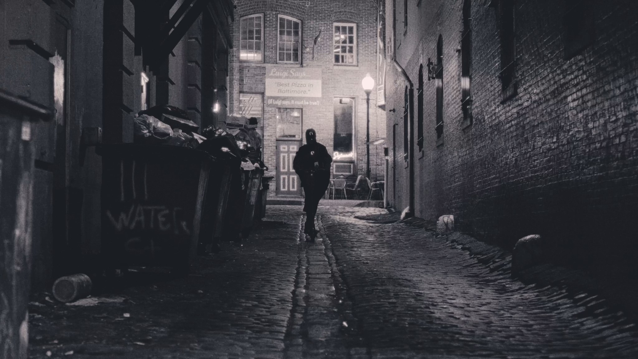 The Raven walking through a wet brick alley in Baltimore at night.